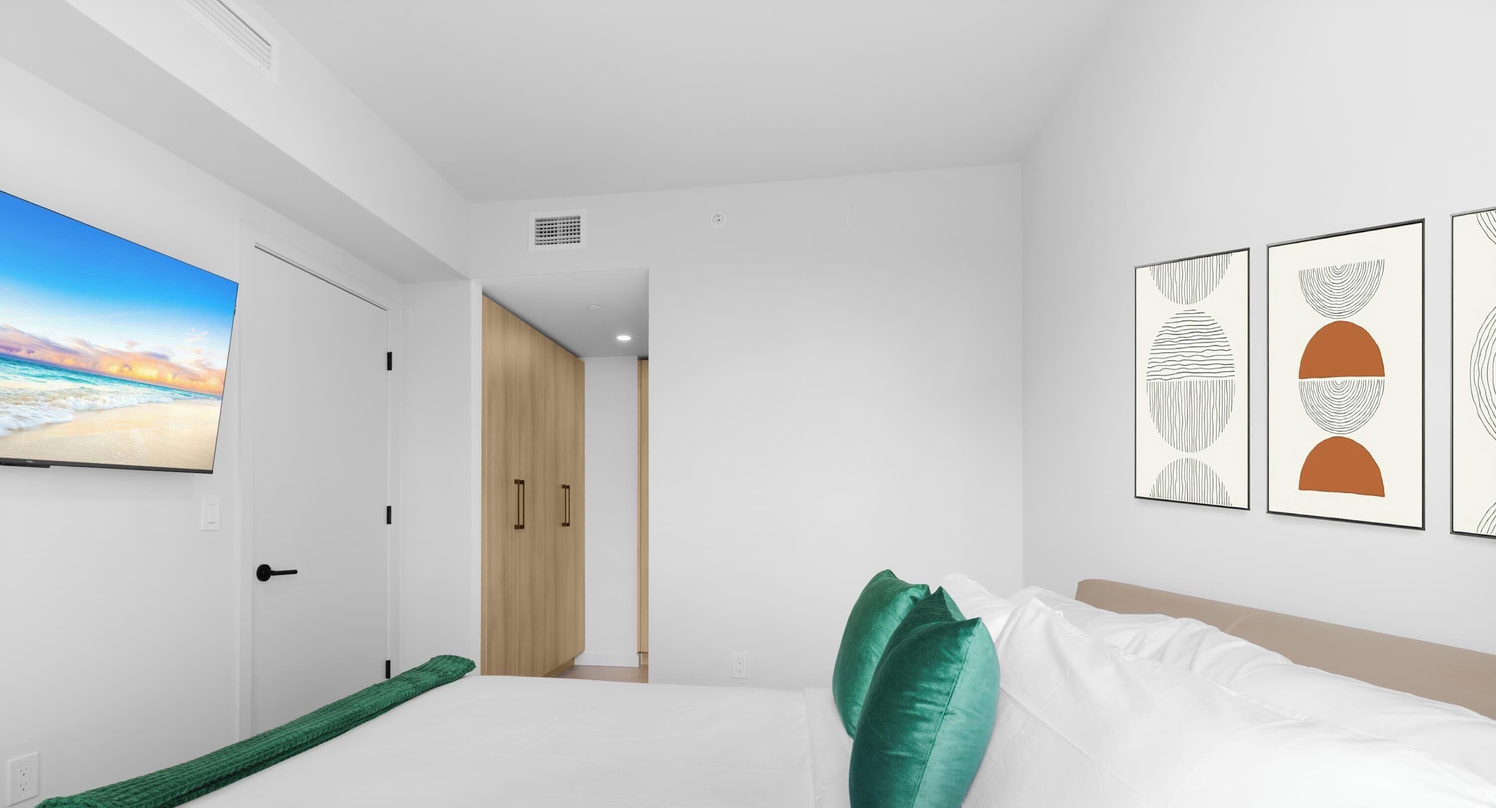 Een moderne slaapkamer met een bed, groene kussens, een televisie aan de muur en abstracte kunst.