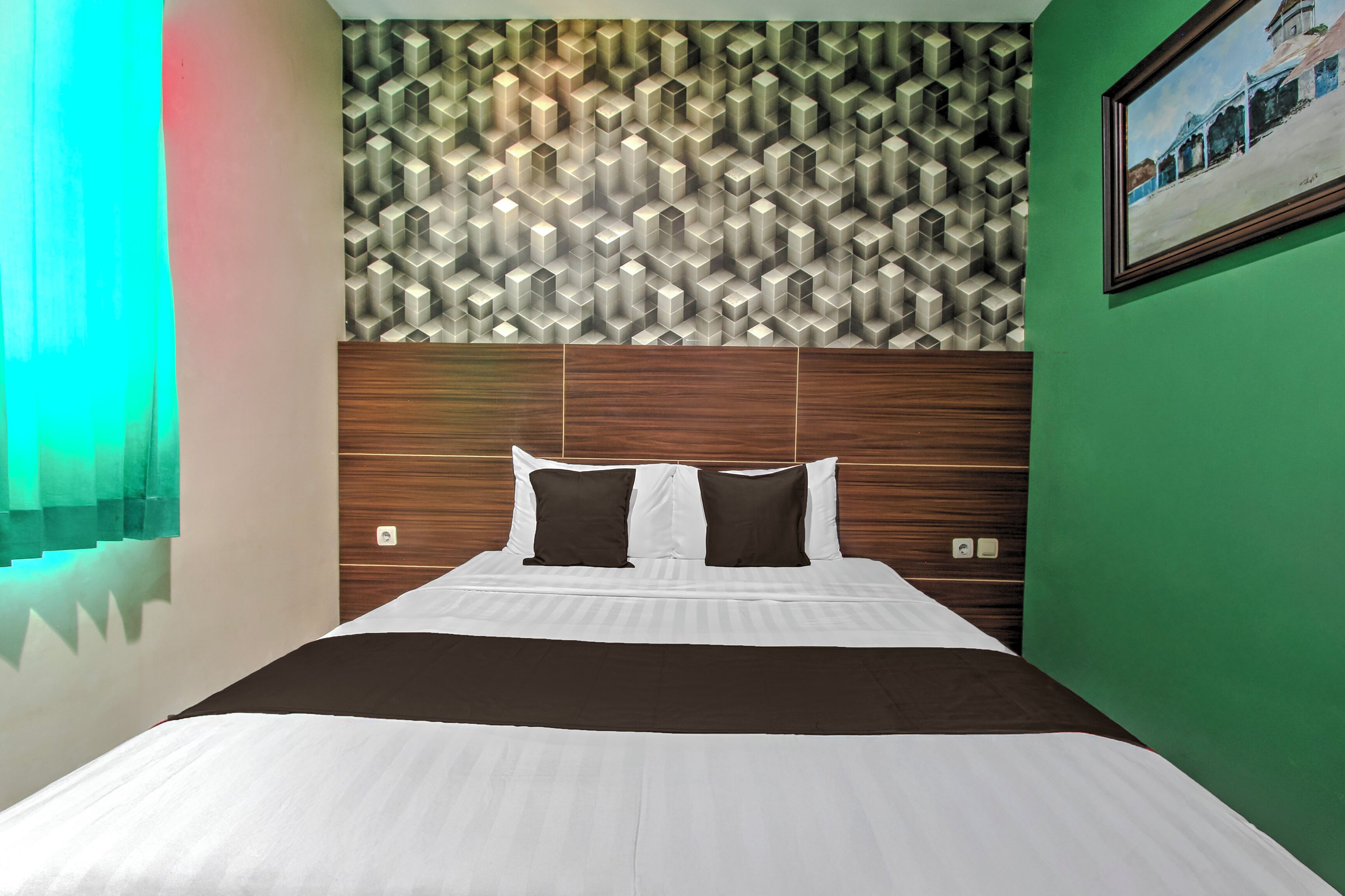 Een hotelkamer met een bed, een patroonbehang, een groene muur en een ingelijst schilderij.