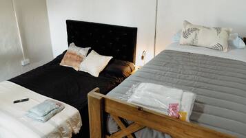 Une chambre avec deux lits, dont l’un a une tête de lit noire et l’autre un cadre en bois. Une table de chevet avec une lampe se trouve à côté du lit de droite.