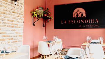 L'intérieur d'un restaurant avec des murs en briques, une enseigne noire portant l'inscription « LA ESCONDIDA », et des tables dressées avec des verres à vin et des assiettes.