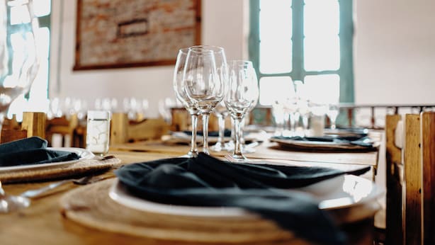 A dining table set with plates, cutlery, and wine glasses, with a window in the background. - Serrano Lodging in the Sierras of Córdoba (Achiras)