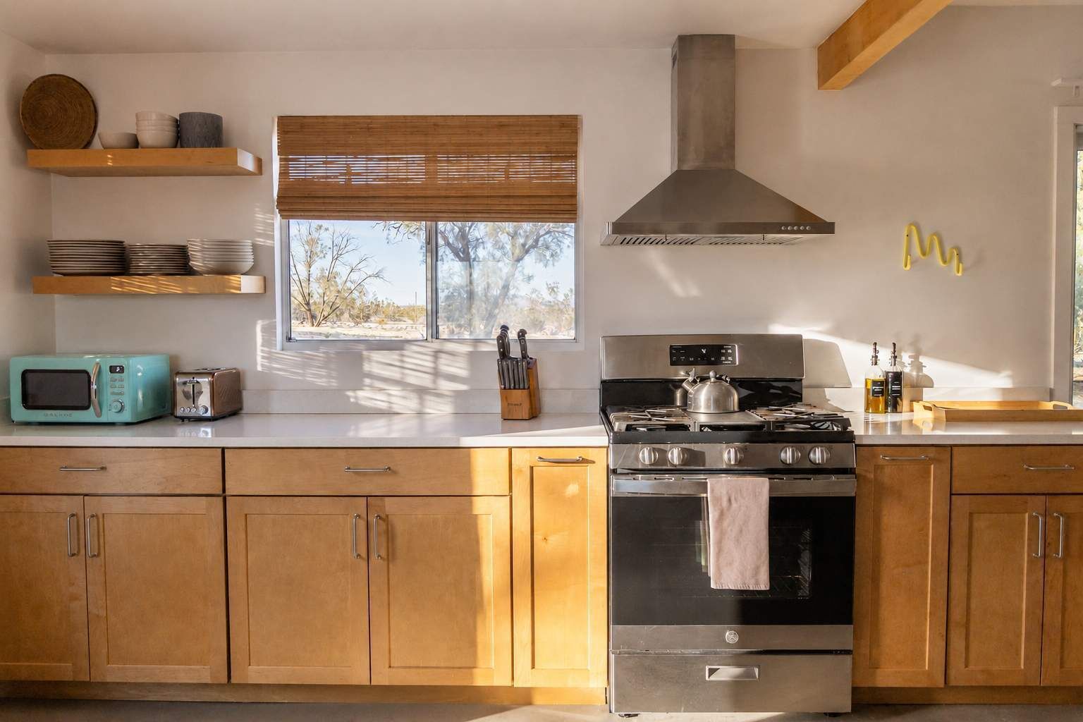 Une cuisine avec des meubles en bois, une cuisinière en acier inoxydable, un four à micro-ondes et une fenêtre avec des stores.