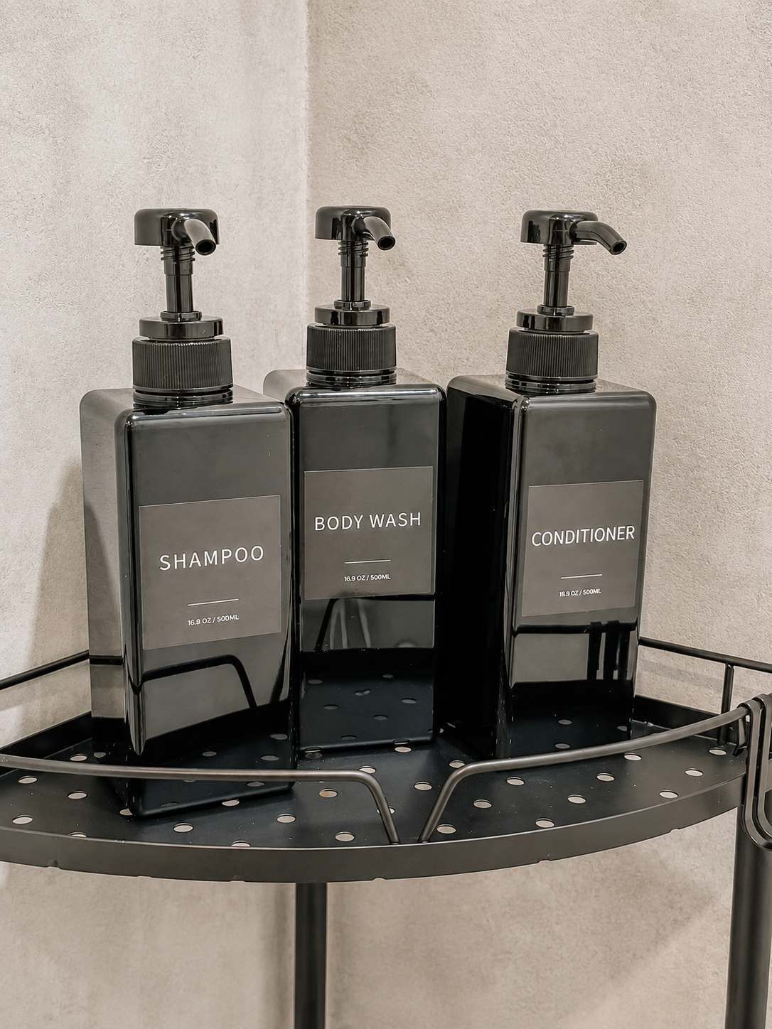 Trois bouteilles noires de produits d’hygiène personnelle sont posées sur une étagère en métal.