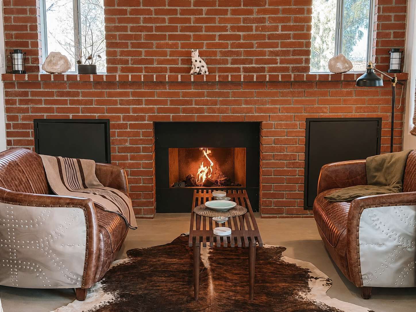 Ein Wohnzimmer mit Kamin aus Backstein, zwei Ledersofas, einem Couchtisch und einem Teppich.