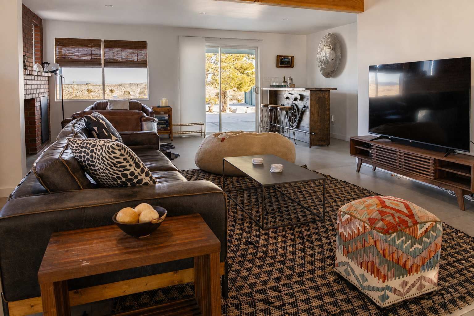 A modern living room with a leather sofa, a coffee table, a television, and a large window with a view of the desert.