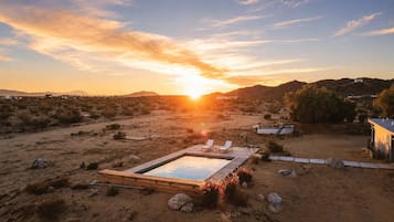 A desert landscape with a swimming pool, lounge chairs, and a small building.