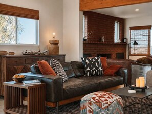 A modern living room with a leather sofa, patterned cushions, a wooden side table, and a fireplace. - Lakeview Lodge • Remote Escape, 5-Acres, Pool, Spa (Joshua Tree)