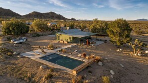 A desert landscape with a swimming pool, a boat, and a small building with a green roof. - Lakeview Lodge • Remote Escape, 5-Acres, Pool, Spa (Joshua Tree)