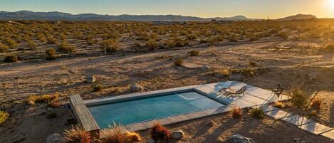 A desert landscape with a swimming pool, lounge chairs, and a clear view of distant mountains.