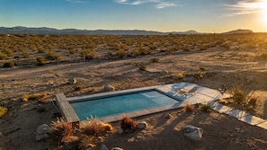 A desert landscape with a swimming pool, lounge chairs, and a clear view of distant mountains. - Lakeview Lodge • Remote Escape, 5-Acres, Pool, Spa (Joshua Tree)