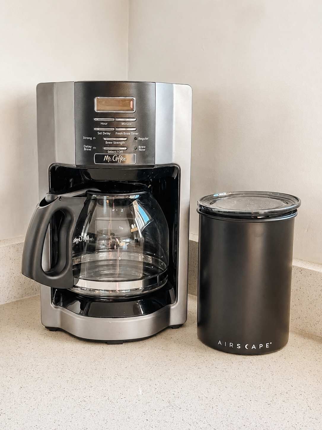 A coffee maker with a digital display and a stainless steel mug beside it.