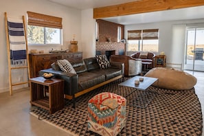 A living room with a leather sofa, a coffee table, a patterned rug, and a fireplace. - Lakeview Lodge • Remote Escape, 5-Acres, Pool, Spa (Joshua Tree)