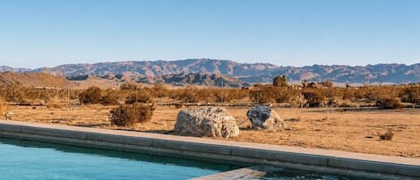 A swimming pool with clear water, surrounded by dry vegetation and mountains in the background.