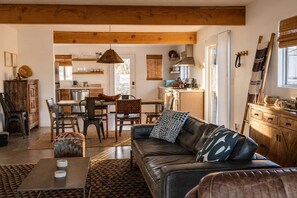 A modern living room with a leather sofa, dining area, and kitchen. - Lakeview Lodge • Remote Escape, 5-Acres, Pool, Spa (Joshua Tree)