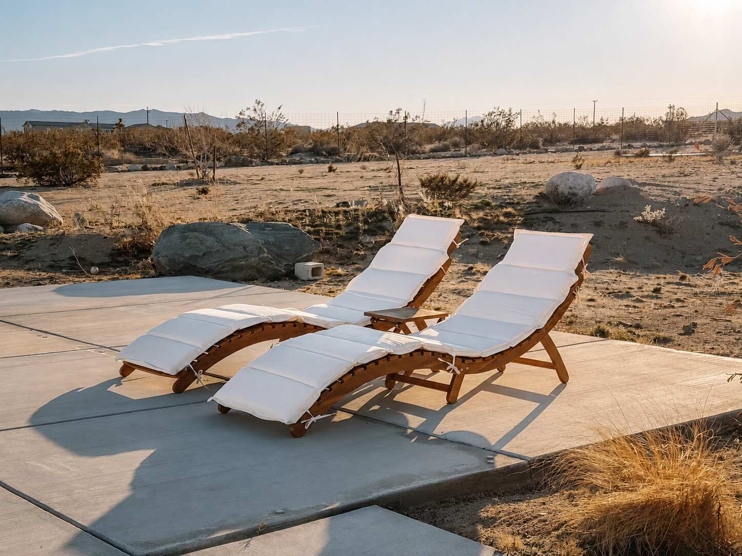 Two wooden lounge chairs with white cushions on a concrete patio.