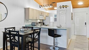 A modern kitchen with wooden ceiling, white cabinets, a central island, and a dining area with a round table and chairs. - Branson Breeze Escape (Branson)