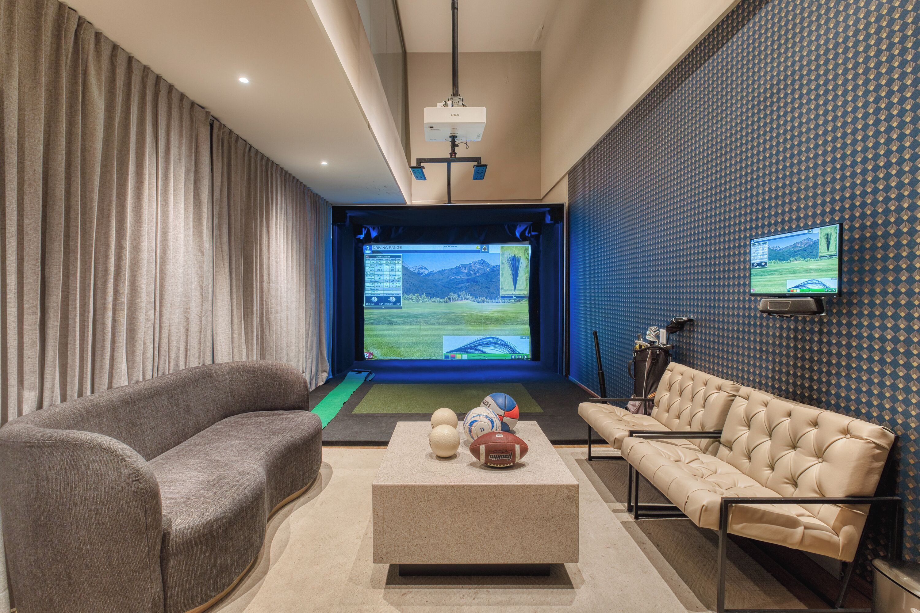 A modern living room with a curved grey sofa, a beige sofa, a coffee table, and a screen displaying a video game.