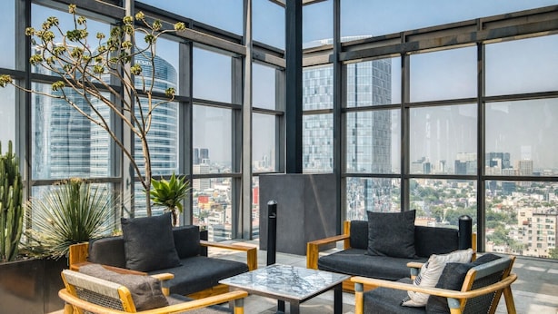 A modern interior with large windows, two sofas, a coffee table, and potted plants. - Nido Reforma (Mexico City)