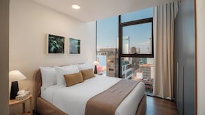 A modern hotel room with a large bed, a nightstand, a lamp, and a view of the cityscape through large windows. - Nido Reforma (Mexico City)