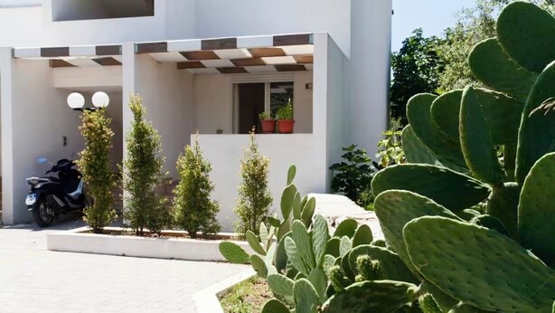 Un edificio moderno con techo plano, un balcón con plantas en macetas y una motocicleta estacionada.
