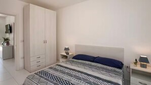 Un dormitorio con cama, mesita de noche, lámpara, armario y una pequeña planta.
