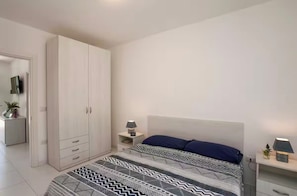 Ein Schlafzimmer mit Bett, Nachttisch, Lampe, Kleiderschrank und einer kleinen Pflanze.