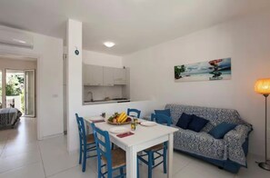 Ein Essbereich mit einem weißen Tisch und blauen Stühlen, einer gemusterten Couch und einem Gemälde an der Wand.