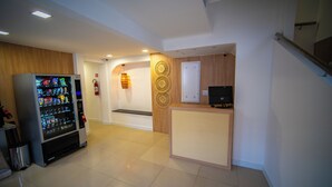 A reception area with a vending machine, a wooden reception desk, and a wall-mounted fire extinguisher. - Amazinn Hotel (Belém)