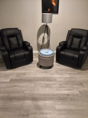 Zwei schwarze Ledersessel, ein kleiner runder Tisch mit blauer Tischplatte und eine Stehlampe mit grauem Lampenschirm.
