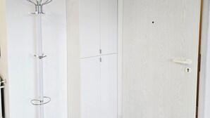 A white wardrobe with a woven basket on top, a coat rack with a decorative branch, and a white door. - Apartment near the clinic (Idar-Oberstein)
