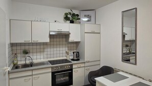 A compact kitchen with white cabinets, a stove, a sink, and a dining table. - Apartment near the clinic (Idar-Oberstein)