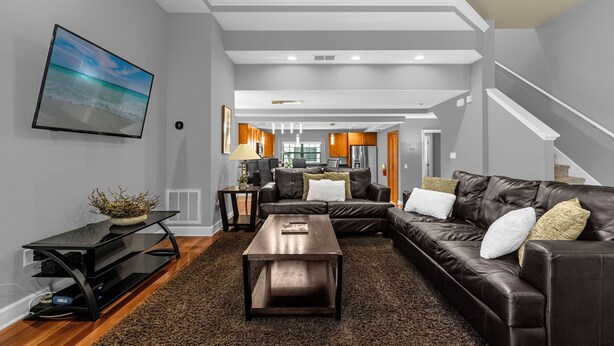 A modern living room with a leather sofa, a coffee table, and a flat-screen TV mounted on the wall. - Enchanted Garden Townhouses  (Orlando)