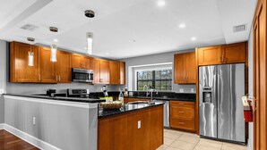 A modern kitchen with wooden cabinets, stainless steel appliances, and a large island. - Enchanted Garden Townhouses  (Orlando)