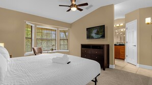 A bedroom with a bed, a ceiling fan, a painting, a dresser, and a bathroom visible through an open door. - Enchanted Garden Townhouses  (Orlando)
