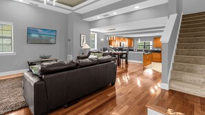 A spacious living area with a dark leather sofa, wooden flooring, and a kitchen in the background. - Enchanted Garden Townhouses  (Orlando)