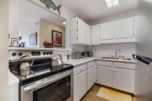 A modern kitchen with white cabinets, a stove, a kettle, a toaster, and a sink. - High-Floor Ocean View in Waikiki | Pool, Free Park (Honolulu)