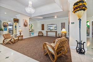 A lobby with a chandelier, wall-mounted artwork, and wicker furniture. - High-Floor Ocean View in Waikiki | Pool, Free Park (Honolulu)