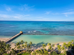 A coastal view with a pier extending into the ocean, palm trees, and clear skies. - High-Floor Ocean View in Waikiki | Pool, Free Park (Honolulu)