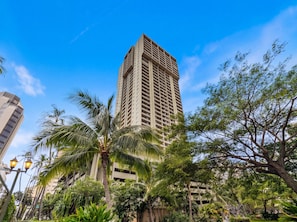 A tall building with a modern design, surrounded by lush greenery and palm trees. - High-Floor Ocean View in Waikiki | Pool, Free Park (Honolulu)