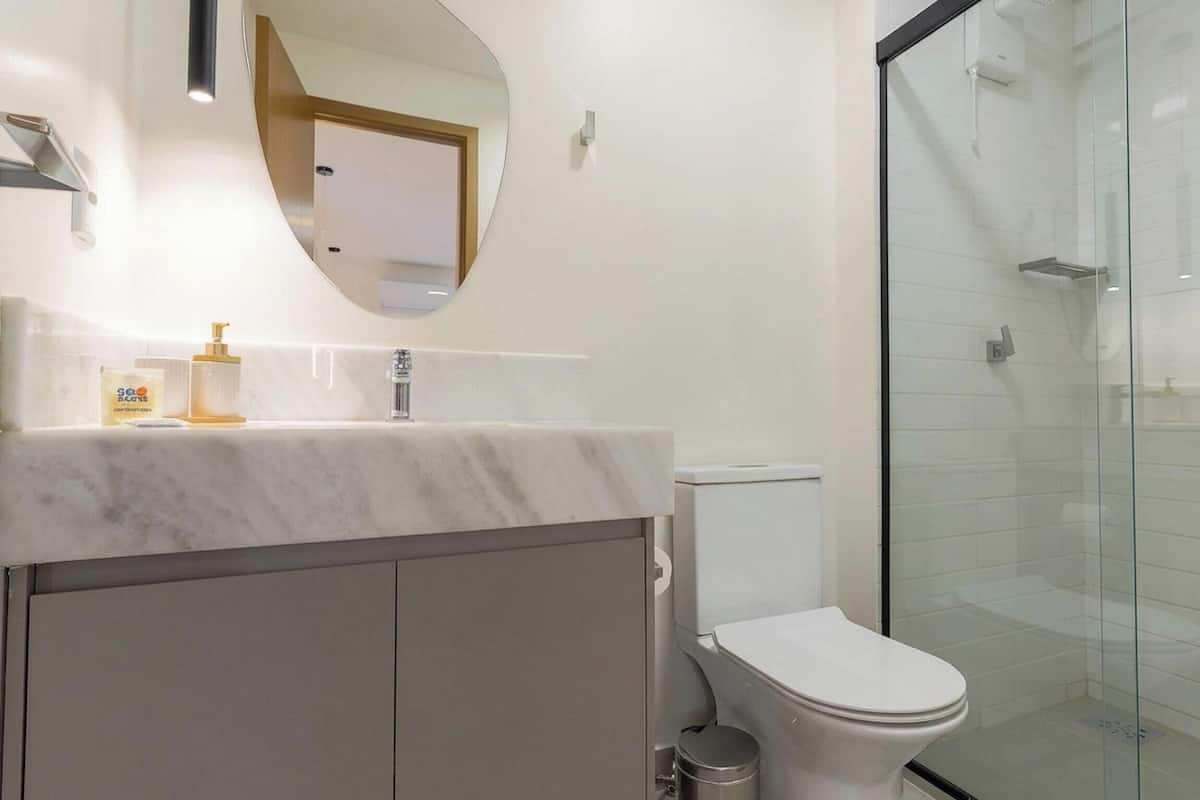 Et moderne badeværelse med en marmorvask, toilet, glasbrusekabine og et spejl med træramme.