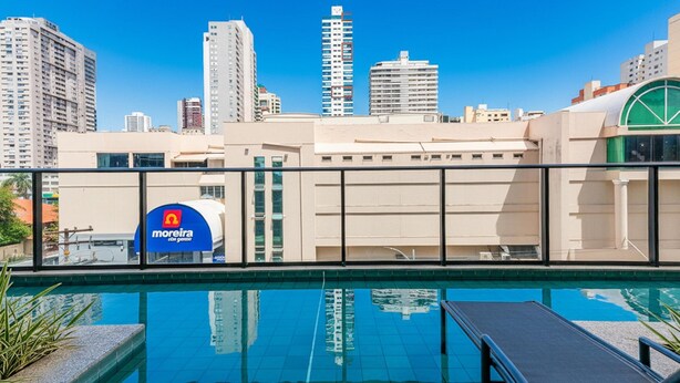 A swimming pool with a cityscape in the background, a 'Moreira' sign, and a building with a green dome. - Apts in a Condo. w/ Pool, a few Steps fr/ Vaca Brava Park - Obds (Goiânia)