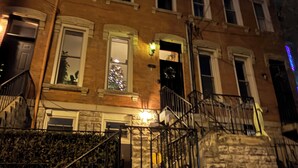 Un immeuble à plusieurs étages, doté d’une façade en pierre, d’un escalier apparent et d’un sapin de Noël visible dans une fenêtre.
