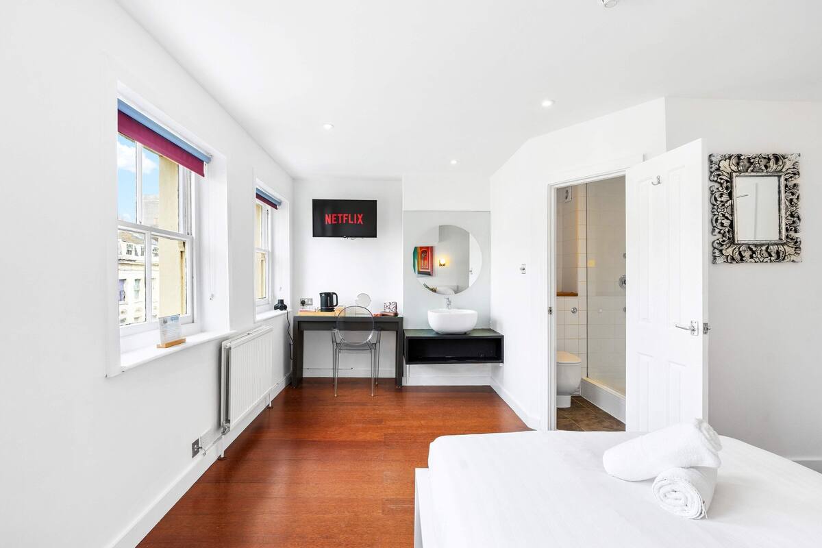 A hotel room with a bed, a desk with a chair, a TV, a bathroom with a toilet, and a shower.