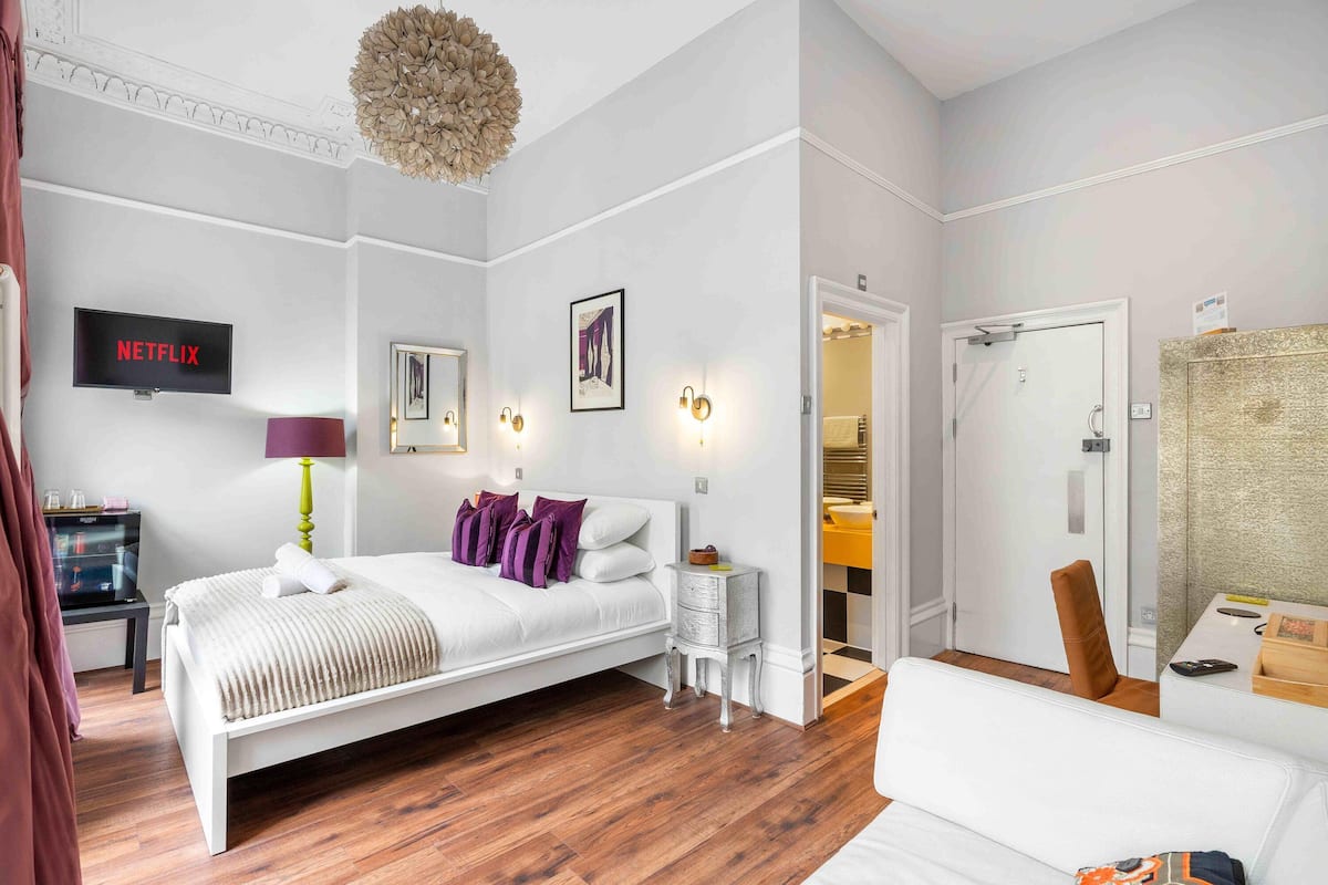 A modern hotel room with a bed, bedside table, lamp, artwork, and a television displaying 'NETFLIX'.