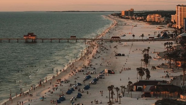 A beach with a pier extending into the water, a sandy shore lined with palm trees, and buildings in the background. - Clean Central Location 3-bedroom 2 Bath house Palm Harbor 1 Block to Starbucks (Palm Harbor)