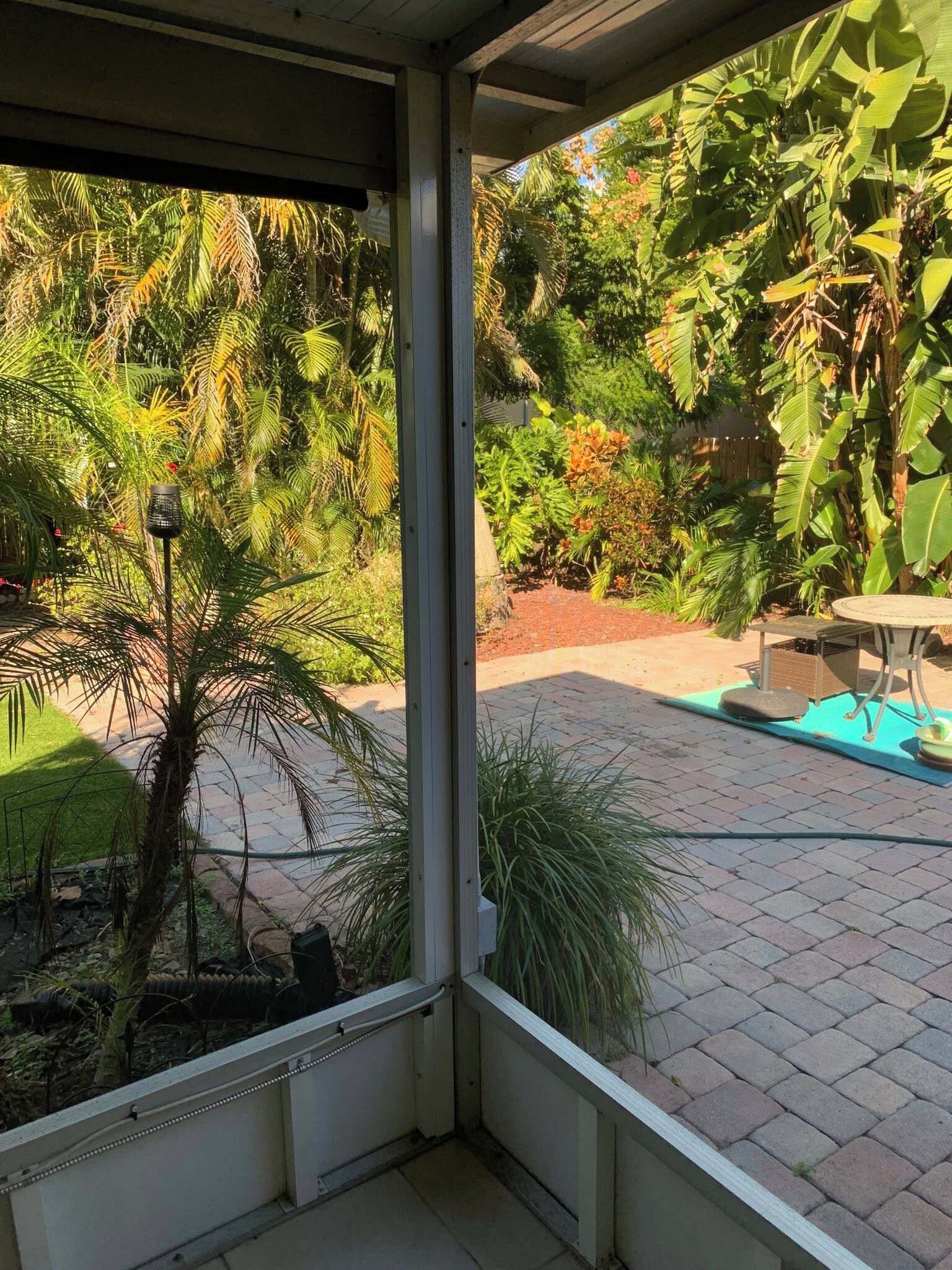 Un patio cubierto con vistas a un jardín, una pequeña mesa y una silla.