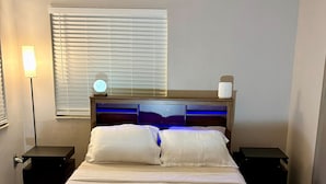 A neatly made bed with a wooden headboard, two bedside tables, a lamp, and a window with blinds. - Clean Central Location 3-bedroom 2 Bath house Palm Harbor 1 Block to Starbucks (Palm Harbor)