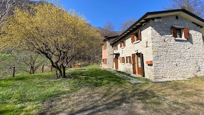 A stone building with a sloped roof, wooden shutters, and a small window.