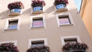 Un immeuble doté de nombreux balcons ornés de jardinières, une entrée centrale avec des arcades et un ciel dégagé au-dessus.