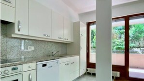 Une cuisine avec des meubles blancs, un plan de travail en granit, un lave-vaisselle et une fenêtre donnant sur un espace verdoyant.